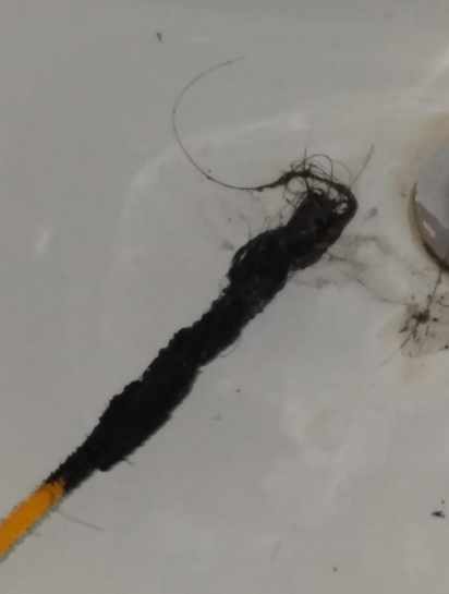 A reviewer demonstrates the gross hair and gunk removed from a drain using the yellow FlexiSnake Drain Millipede.
