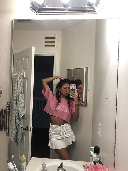 A reviewer sporting a white ruched skirt paired with a pink cropped t-shirt for a stylish and casual look.