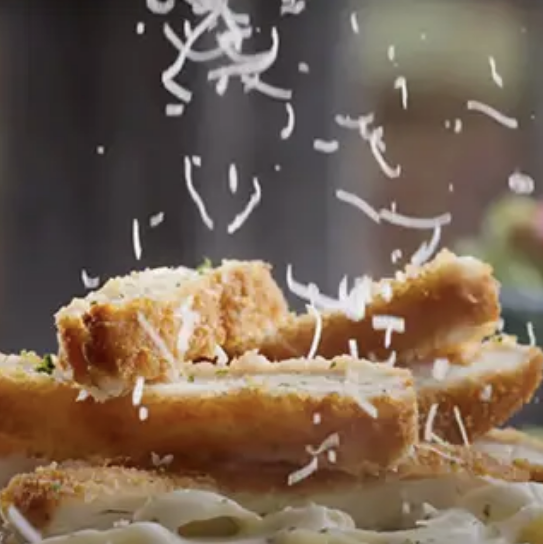 Cheese being grated onto a chicken pasta dish