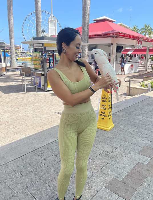A reviewer sporting the same snakeskin-print set in a light green color while enjoying time at the beach
