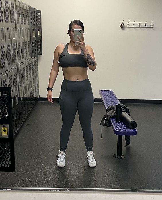 The reviewer is dressed in grey leggings, white sneakers, and a matching grey sports bra