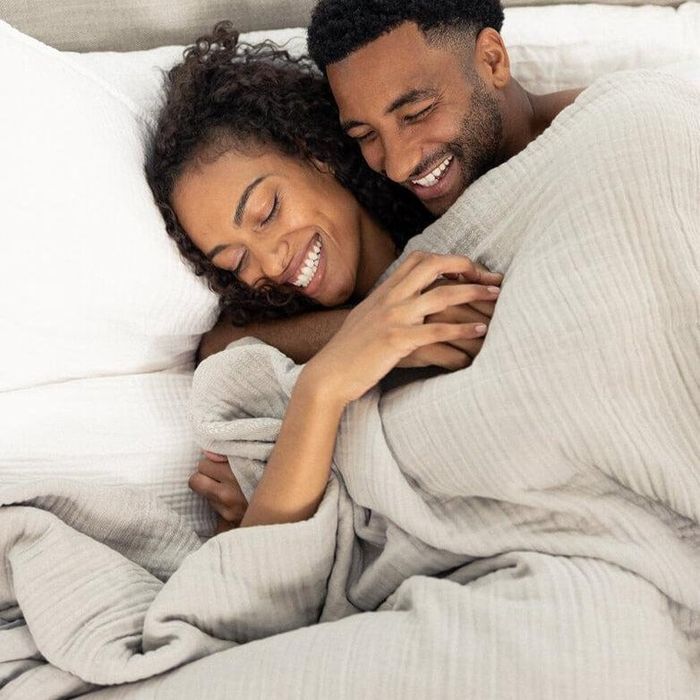 A couple shares a smile and snuggles in bed beneath a soft blanket, exuding a sense of comfort and relaxation—ideal for an article about bedding or sleepwear.