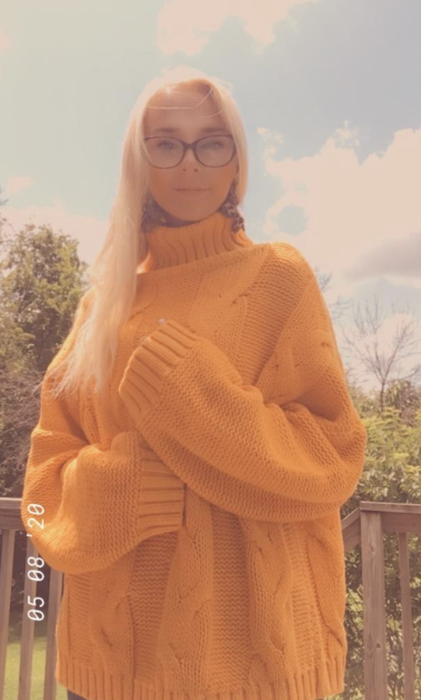 A reviewer models the oversized yellow knit sweater, embracing its bold and cozy design.