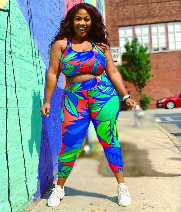 A model sporting vibrant, tropical flower-print workout leggings in red, blue, and green, featuring a high-rise waistband