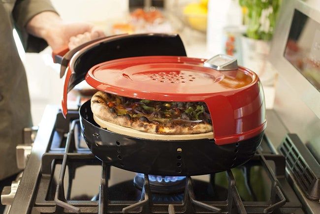 a pizza baking in the stove-top pizza oven, perched atop a gas burner