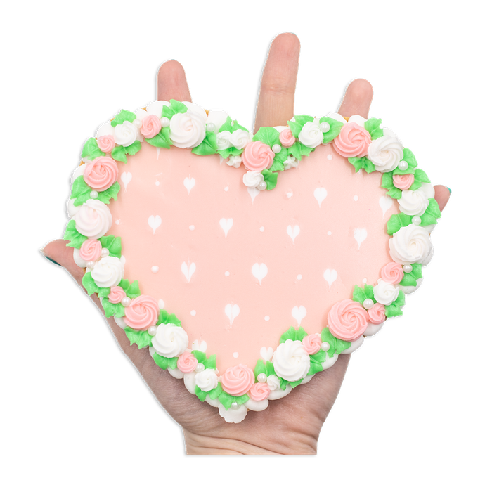 A heart-shaped cookie with delicate floral piping around the edges and pink frosting adorned with tiny hearts