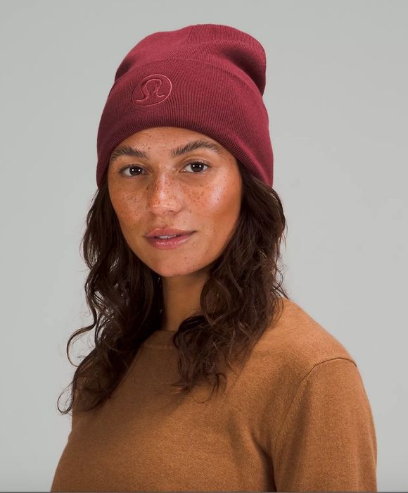 Model wearing a deep red beanie featuring the Lululemon logo embroidered on the front