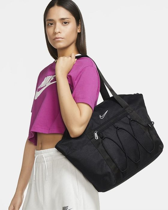 A model carrying a black tote bag, paired with a pink cropped tee and white sweatpants