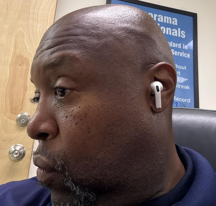 Person seated indoors, wearing wireless earbuds, absorbed in focus. A poster hangs in the background.