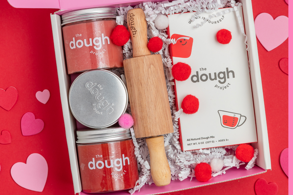 Three jars of all-natural play dough, a small wooden rolling pin, and a DIY kit to create custom dough.
