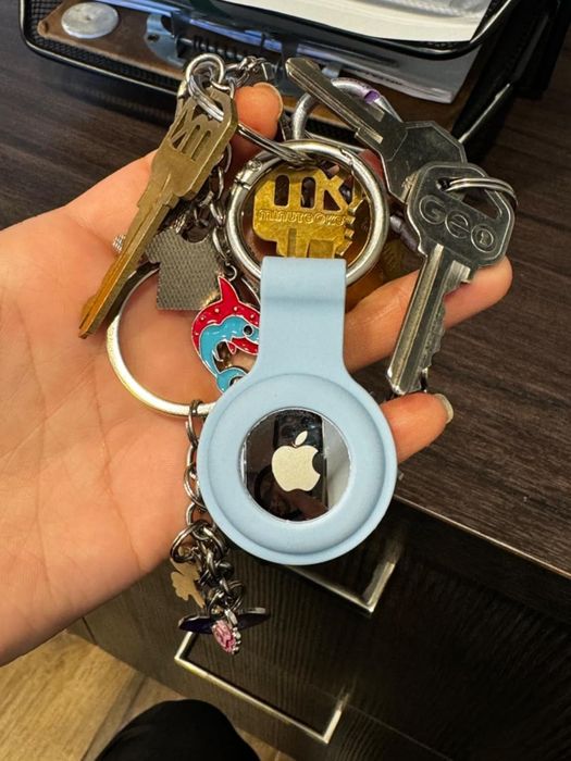 A close-up shot of a hand clutching a set of keys, one of which is an Apple AirTag.