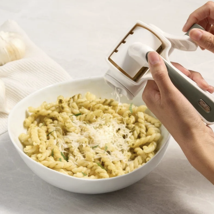 Someone grating cheese onto a pasta dish