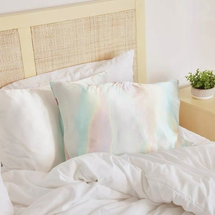A bed with crisp white sheets, paired with a colorful pillowcase and a small potted plant on the bedside table.