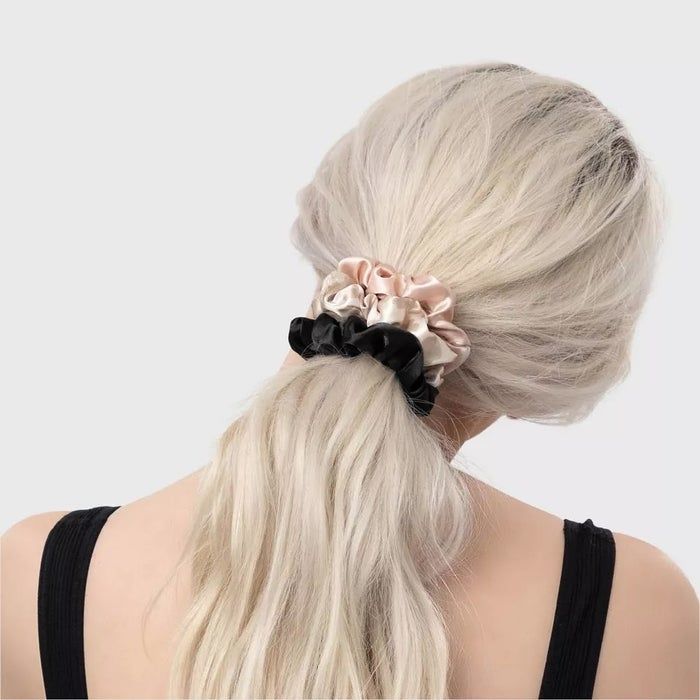 A woman with long blonde hair, simply styled with silk scrunchies, wearing a black top.