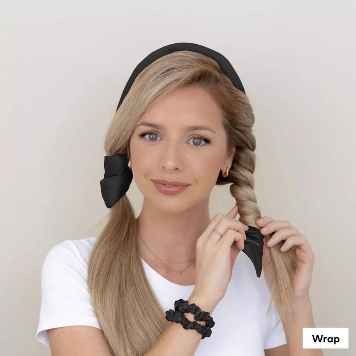 A woman with blonde braided hair wears accessories in her hair, paired with a white top and black scrunchies on her wrists.