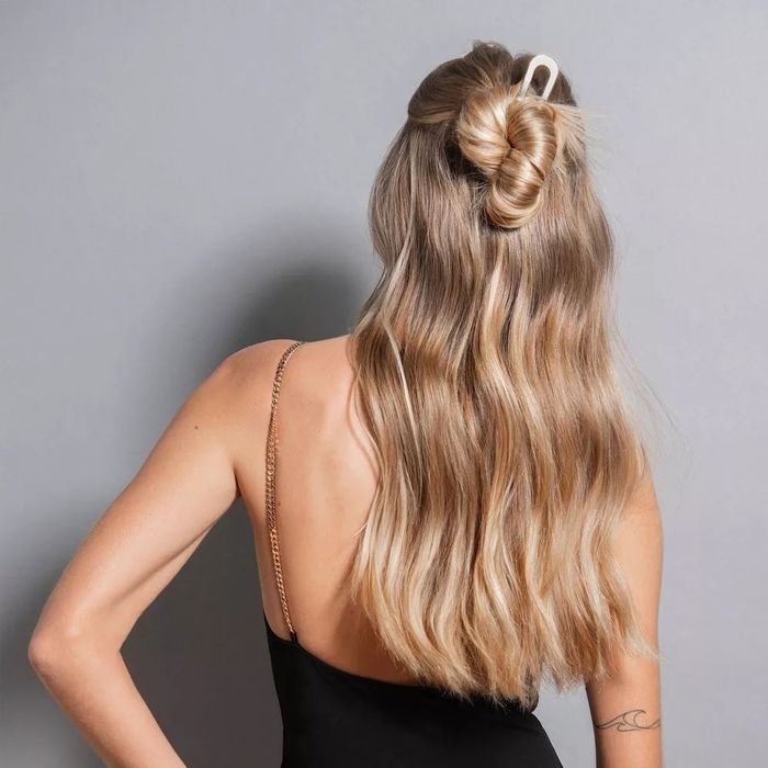 A woman with long hair styled in a twisted bun, dressed in a strappy black top, displaying a small tattoo on her back.