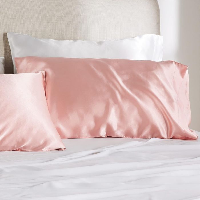 Two pillows with coral silk pillowcases placed on a bed.
