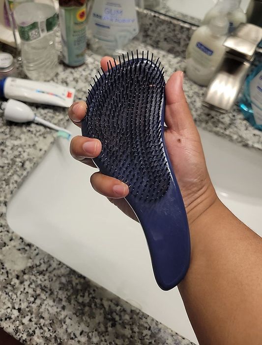 A reviewer holding a turquoise-colored detangling brush in hand.