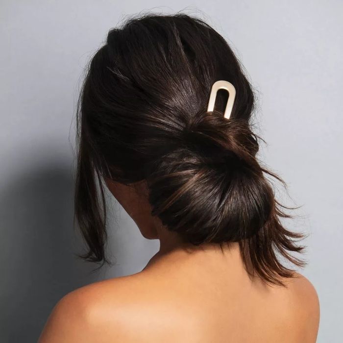 A person with dark hair styled into a low bun, held in place with a sleek, minimalist hair clip. The person's face is not visible.