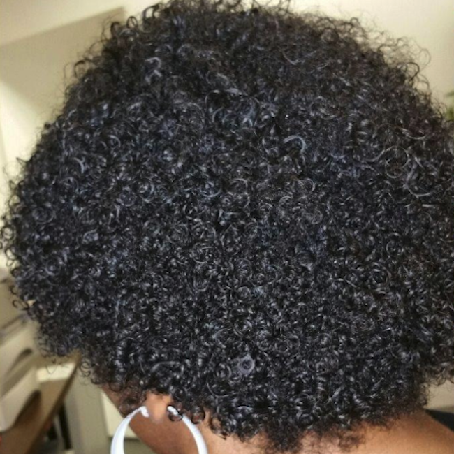 A woman with short, 4A curly hair that has been detangled, showing beautifully defined curls.