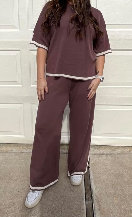 A woman wearing a stylish two-piece loungewear set with white trim, standing casually in front of a door