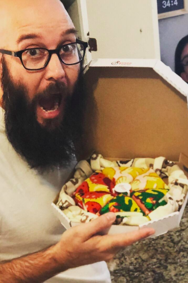 A reviewer holding a pizza box filled with socks that resemble a pizza.