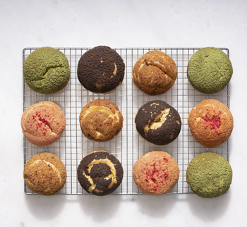 A variety of cream puffs, each with its own unique flavor, resting on a cooling rack.