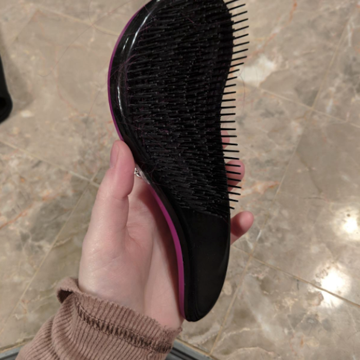 A detangling brush with a curved 'S' shape, featuring bristles that cover the entire surface.
