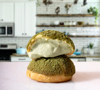 stacked matcha cream puffs, one open to reveal its filling