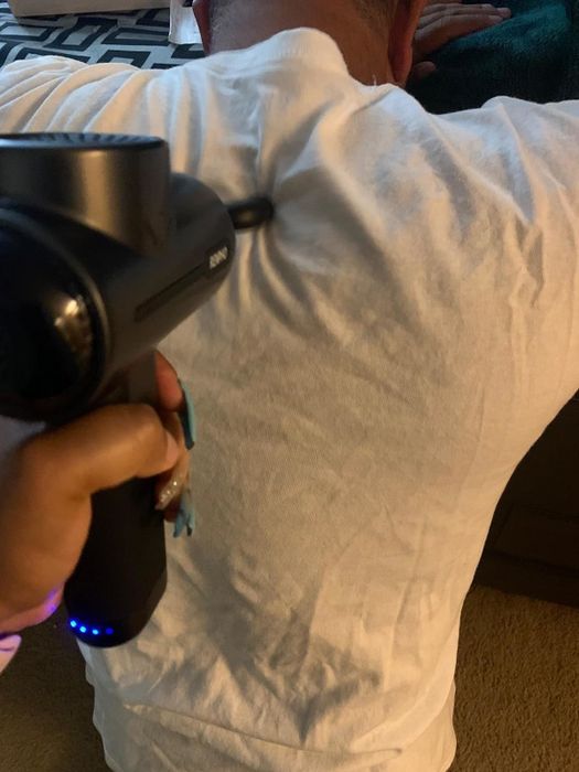 A reviewer’s photo showing the massage gun being applied to someone’s back for relief.