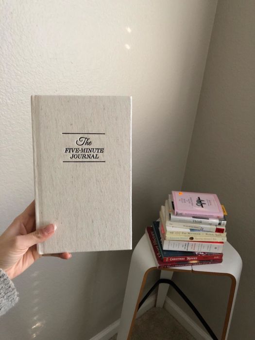 A reviewer holding up the white journal in front of their book collection