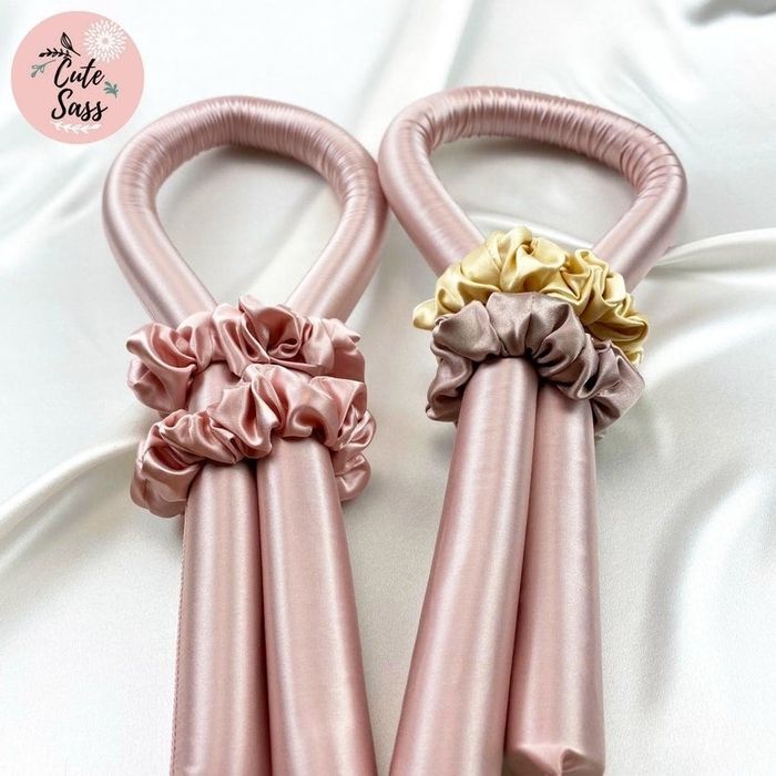 Two pink curling wands with scrunchies wrapped around them.