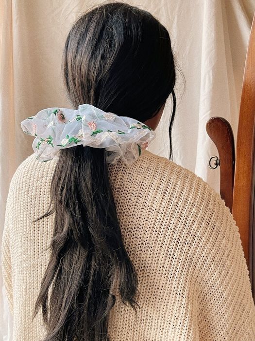 A model wearing a sheer, embroidered floral organza scrunchie.