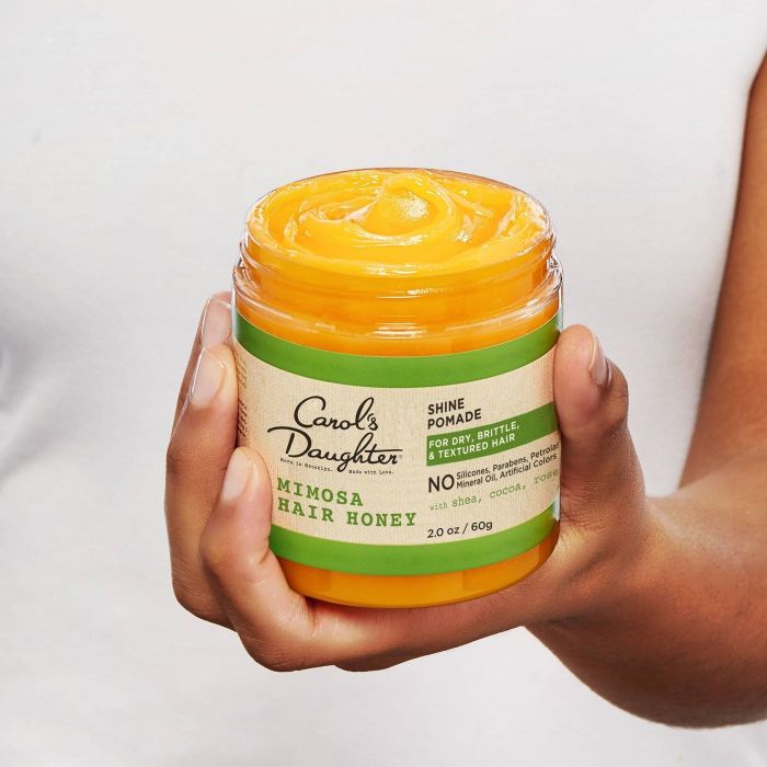 Hand holding a jar of thick, yellow, whipped treatment.