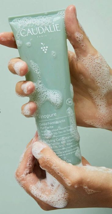 Hands holding the Caudalie Vinopure Purifying Gel Cleanser, now coated with a rich foamy lather, demonstrating its use for effective cleansing.
