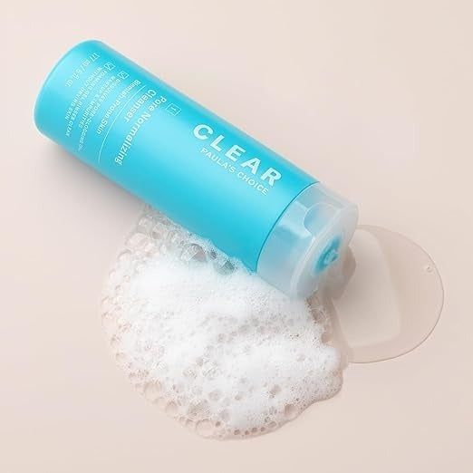 A bottle of Paula's Choice Clear Cleanser resting on its side with some of the frothy cleanser spilling onto the surface.