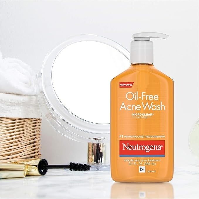 Neutrogena Oil-Free Acne Wash with salicylic acid placed on a bathroom counter, beside a mirror, a brush, and towels in a wicker basket.