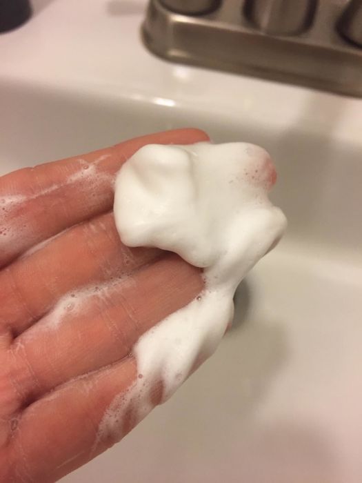 A hand of a reviewer holding the foamy cleanser