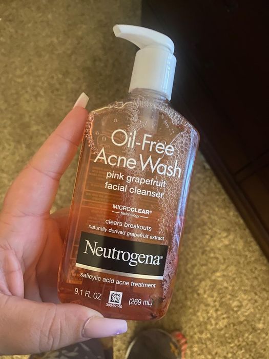 A hand holding a bottle of Neutrogena Oil-Free Acne Wash Pink Grapefruit Facial Cleanser, formulated with salicylic acid to combat breakouts.