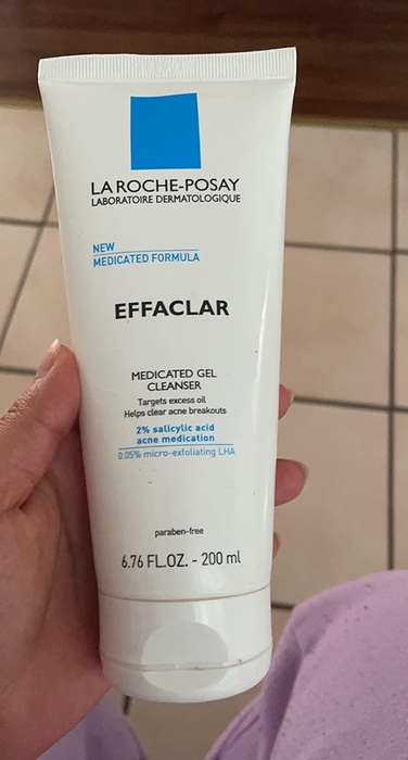 A reviewer holds the tube of La Roche-Posay Effaclar Medicated Gel Cleanser, highlighting its ability to clear acne with 2% salicylic acid and 0.05% LHA.