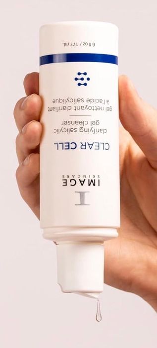 A hand holds a bottle of IMAGE Skincare Clear Cell Clarifying Salicylic Gel Cleanser, dispensing a small drop of product