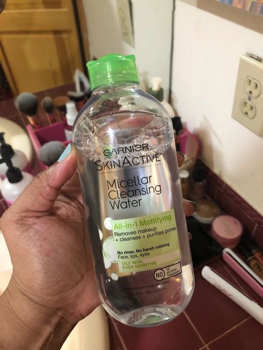 A reviewer showcasing the bottle, which claims it is ideal for oil and sensitive skin