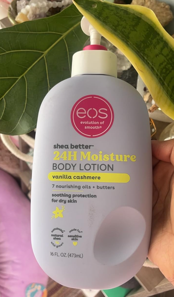 A person holding the Eos Shea Butter 24H Moisture Body Lotion bottle