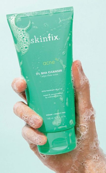 A hand, lathered in foam, holds a tube of Skinfix acne+ 2% BHA Cleanser, a vegan and cruelty-free product designed to help clear acne