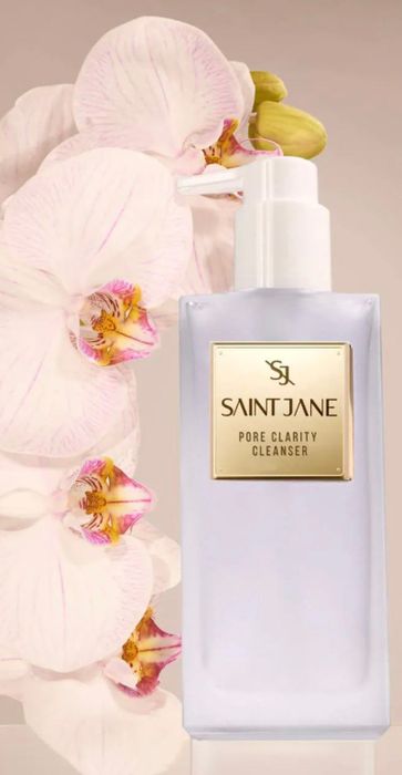 A bottle of Saint Jane Pore Clarity Cleanser placed in front of elegant white orchids.