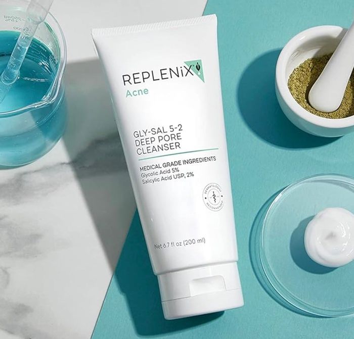 The Replenix Acne Gly-Sal 5-2 Deep Pore Cleanser tube is displayed alongside skincare tools and ingredients, emphasizing its medical-grade glycolic and salicylic acid components