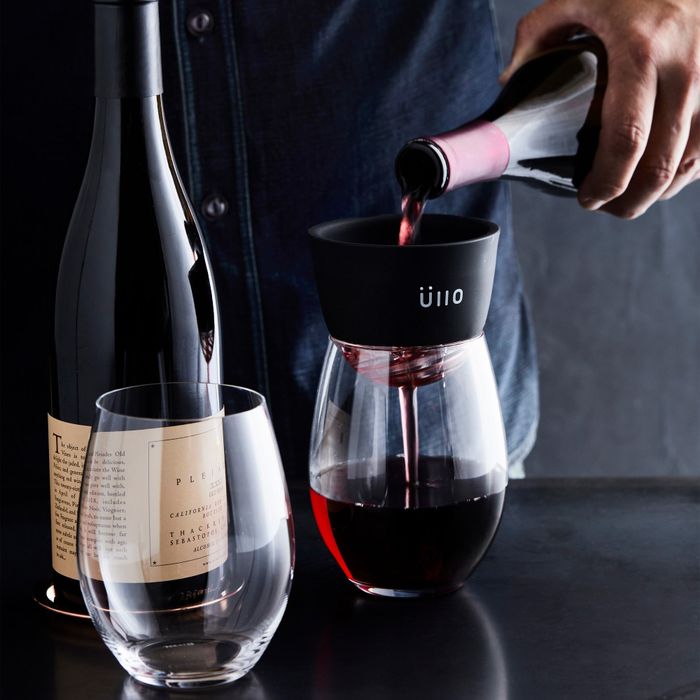 A person pouring red wine through the Ullo purifier into wine glasses.