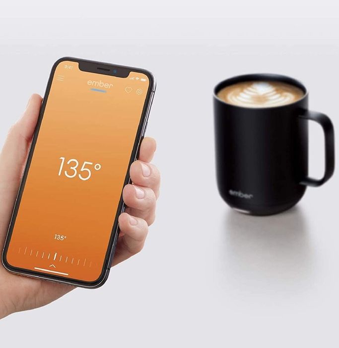 A model holding a smartphone in front of the Ember mug with the app visible on the screen