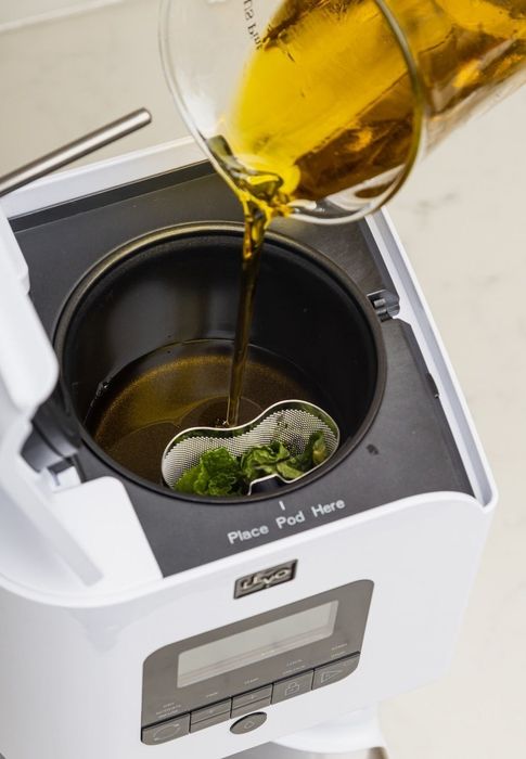 Herbs are added to the oil being poured into the white Levo, preparing for infusion.