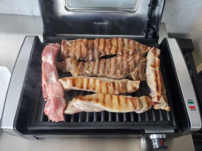 A reviewer demonstrates the grill in action, sizzling meat as it cooks.